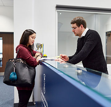 Student talking to a member of the Student Life and Education Services Team at The College's reception desk.