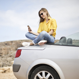 Girl in yellow t-shirt sitting on the back of a convertible car looking at her mobile phone